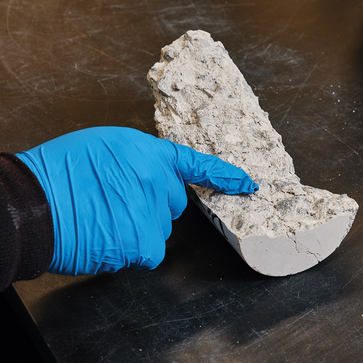 a gloved hand pointing into the rough interior of a broken cement cylinder