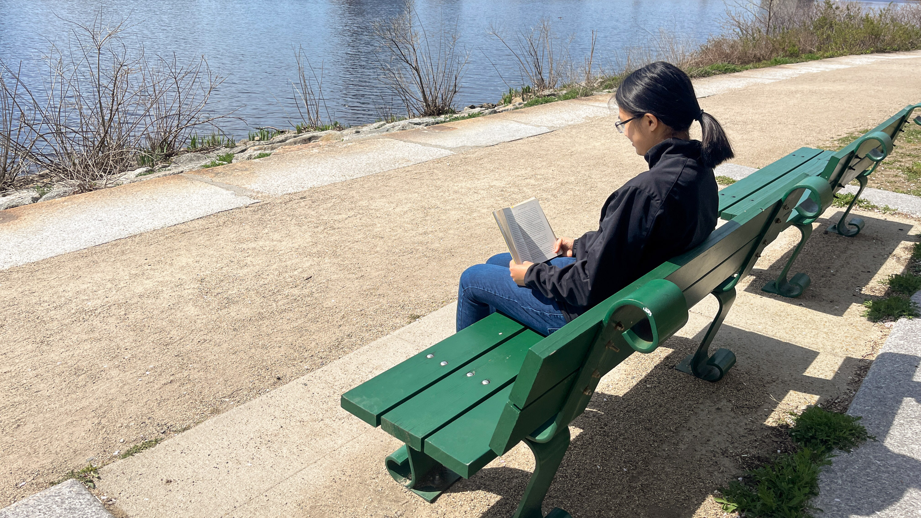 Vivian Hir sitting on a park bench by the Charles River